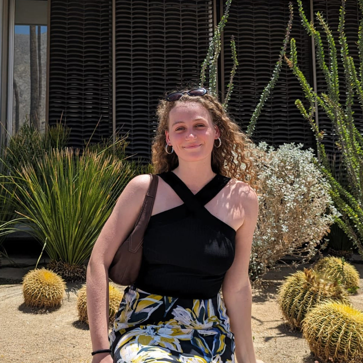 Woman sitting on a wall in front of a modern house with cacti and succulents.